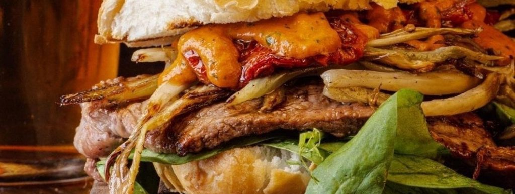 Sandwich de picaña braseada con sal roja con cebollas asadas y mayonesa de pimientos asados y hojas verdes
